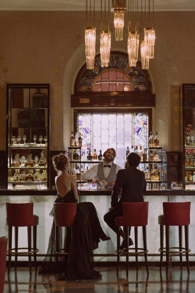 Heiratsantrag /Proposal Page 6 A couple enjoying a drink at a luxurious bar with a friendly bartender, set in an elegant interior.